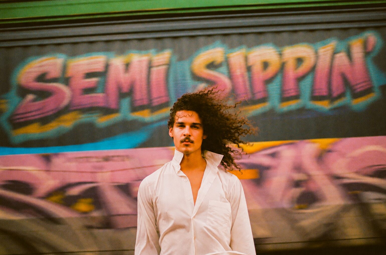 Semi Sippin' painted across a passing freight car, a man in a white shirt in front of it